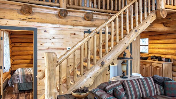 A log cabin interior with a wooden staircase, a sofa, and a small table with a bowl. - Spring Pond Cabin at White Buffalo Lodge;
Family-sized with lake access (Grove)