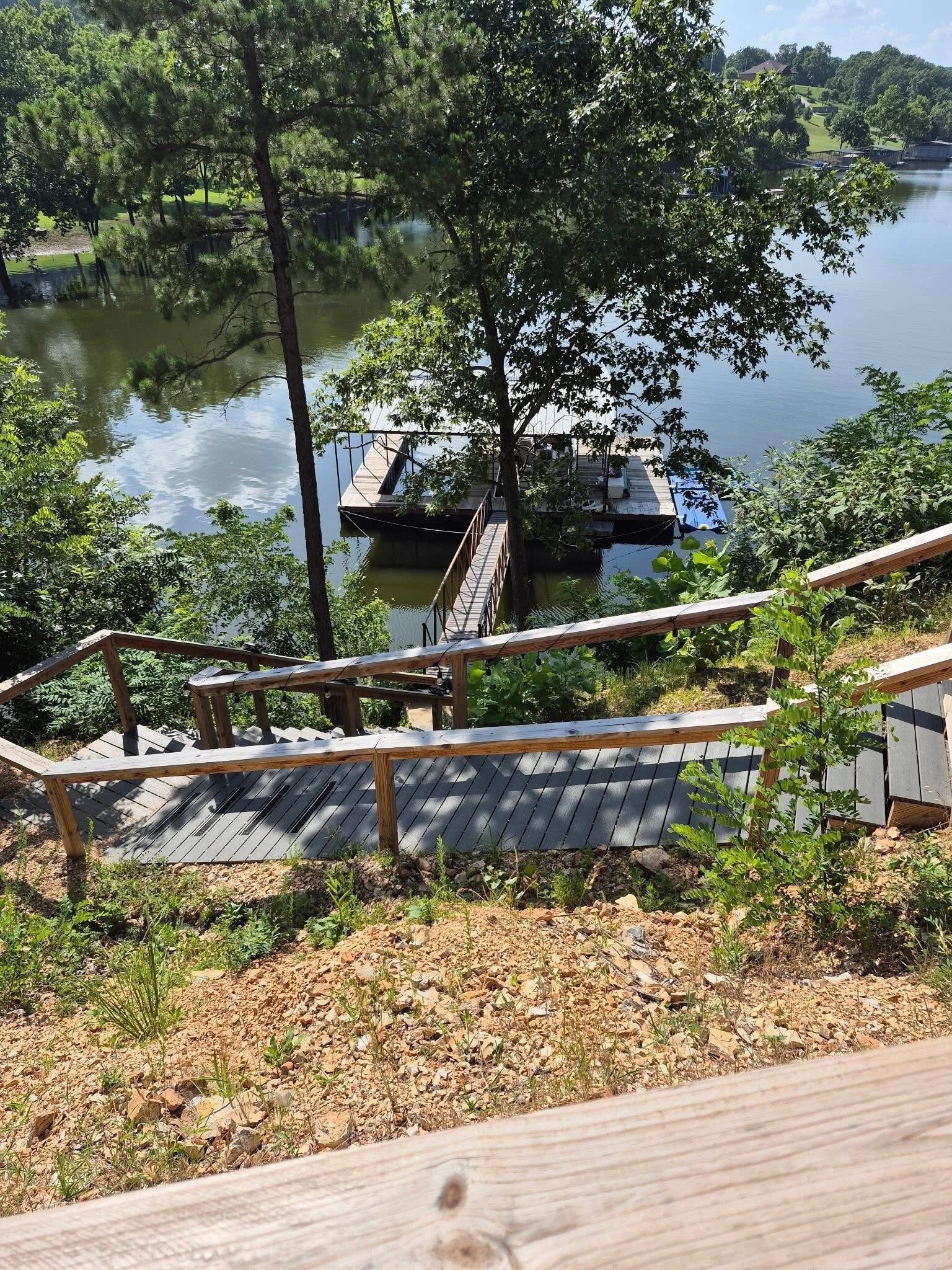 A wooden deck leading to a dock over a calm lake, surrounded by trees and greenery.