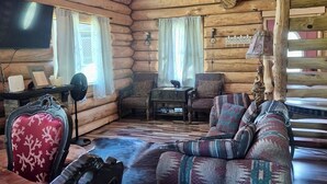 A log cabin interior with a sofa, armchair, and a small table with a lamp. - Spring Pond Cabin at White Buffalo Lodge;
Family-sized with lake access (Grove)