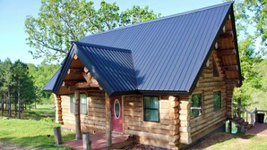A log cabin with a metal roof, wooden exterior, and a red door. - Spring Pond Cabin at White Buffalo Lodge;
Family-sized with lake access (Grove)