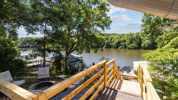Une terrasse en bois avec une balustrade donnant sur un lac, entourée d’arbres.