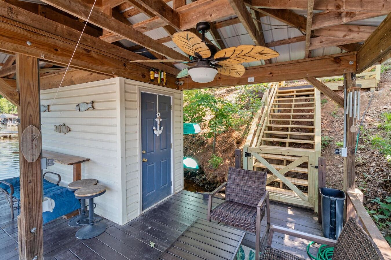 A covered outdoor deck with a ceiling fan, a door, and a small table with stools.