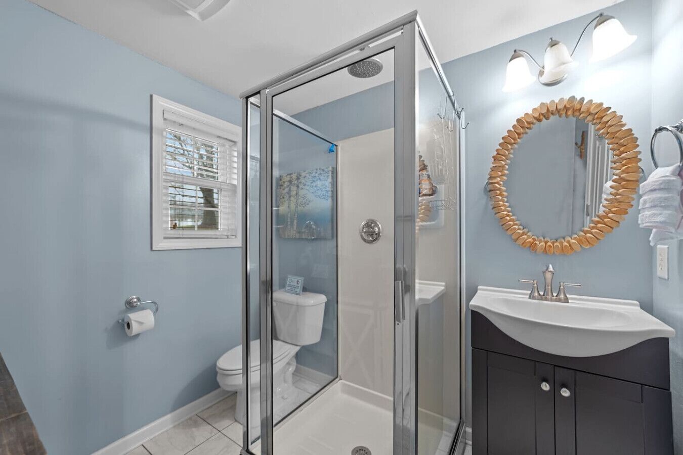 A bathroom with a glass-enclosed shower, a white toilet, a sink with a wooden mirror, and a towel rack.