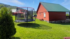 Een trampoline in een gazon, met een rode schuur op de achtergrond.