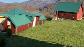 Ein rotes Backsteinhaus mit grünem Dach und ein kleineres Gebäude daneben, umgeben von einer Wiese und Bergen im Hintergrund.