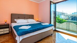 A bedroom with a large bed, a nightstand, and a view of a building through a glass door. - Two Bedroom Apartment with Terrace (Ugljan)