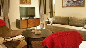 A living room with a sofa, two armchairs, a TV on a wooden cabinet, and two paintings on the wall. - Luxury Style Apartments - Studio Apartment (Elegant) (Dubrovnik)