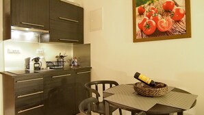 A modern kitchen with dark cabinets, a stainless steel sink, and a dining area with a table and chairs. - Luxury Style Apartments - Studio Apartment (Elegant) (Dubrovnik)