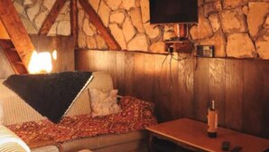 A cozy room with a stone wall, a wooden ceiling, a bed with a patterned blanket, and a table with a bottle.