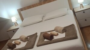 Una cama bien hecha con almohadas y toallas ordenadas sobre ella. Hay dos mesitas de noche con lámparas.