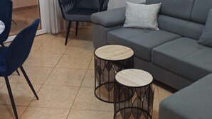 Una sala de estar moderna con un sofá gris, dos mesitas redondas, un sillón azul oscuro y una pequeña mesa redonda con base de diseño floral.
