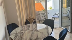 Un comedor con una mesa de mármol, sillas negras y un jarrón con flores secas.