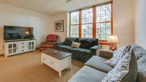 A living room with a television, sofa, and a window with a view of trees.