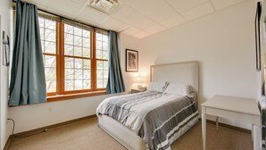 A bedroom with a bed, a bedside table, a nightstand, a window with curtains, and a framed picture on the wall.