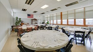 A spacious dining area with multiple round tables set for meals, featuring white tablecloths and neatly arranged cutlery.