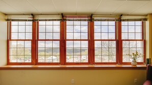 A room with a large window with multiple panes, a chair, and a vase with flowers on the windowsill. - Day Trip to Pittsburgh: Comfy New Kensington Apt! (New Kensington)
