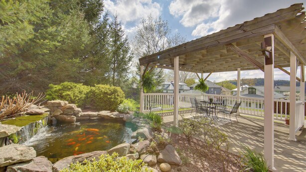 A covered patio with outdoor furniture, a koi pond, and surrounding greenery. - Day Trip to Pittsburgh: Comfy New Kensington Apt! (New Kensington)