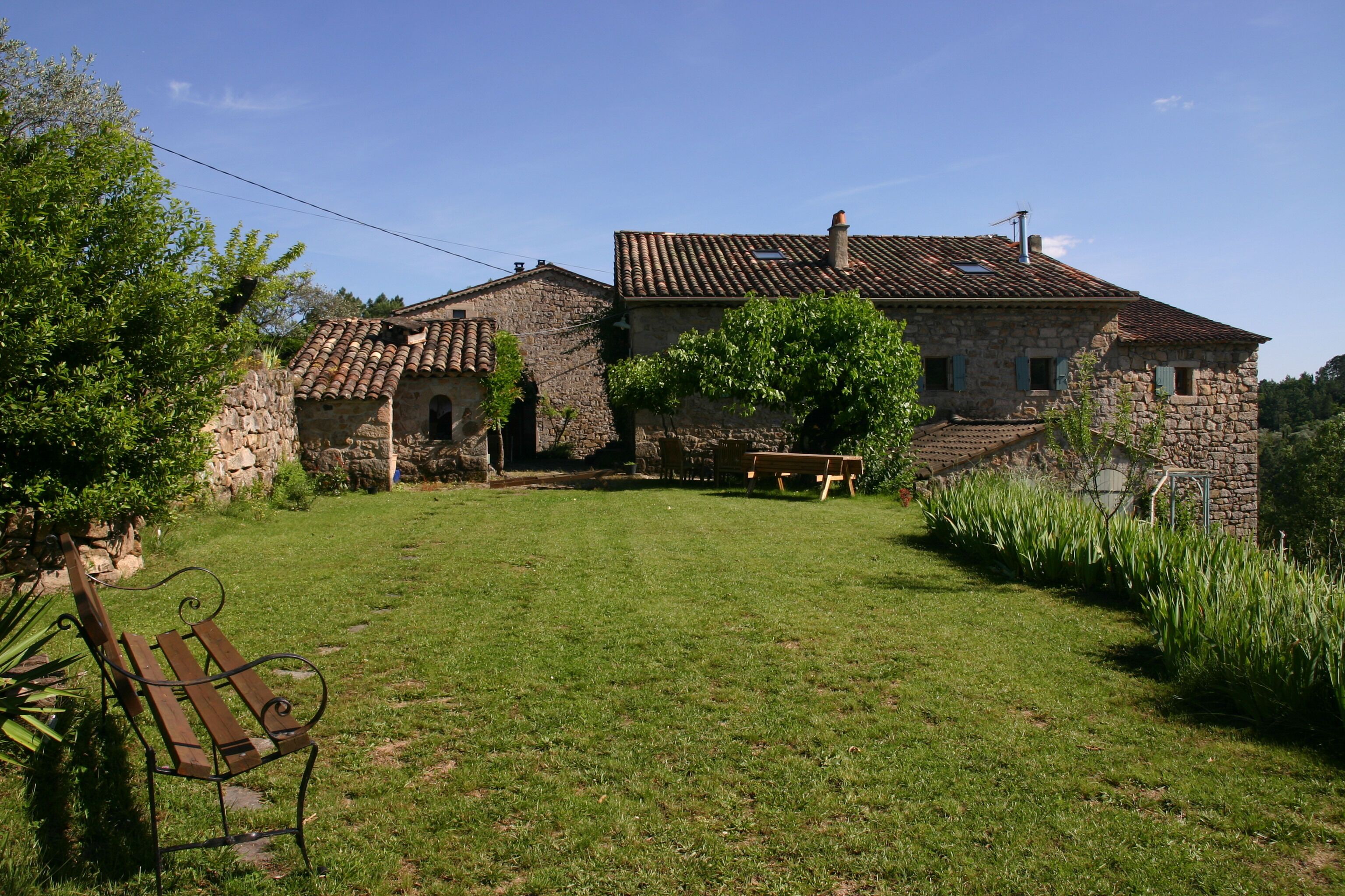 A stone house with a tiled roof, a grassy yard, and a bench.