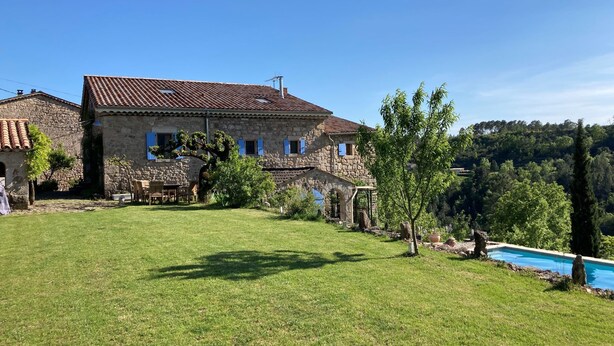 Una casa de piedra con tejado de baldosas, piscina y césped bien cuidado.