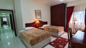 A hotel room with two beds, a desk, and a chair. There is a door leading to another room and a hallway. - Ivory Hotel Apartment (Abu Dhabi)
