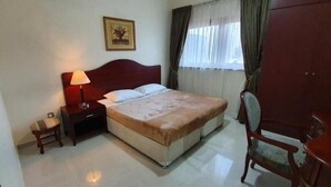 A hotel room with a bed, a nightstand with a lamp, a chair, and a wardrobe. - Ivory Hotel Apartment (Abu Dhabi)