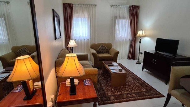 A hotel room with a sofa set, two lamps, a TV, a desk with a telephone, and a decorative rug. - Ivory Hotel Apartment (Abu Dhabi)