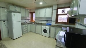 A compact kitchen with white cabinets, a washing machine, and a microwave. - Ivory Hotel Apartment (Abu Dhabi)