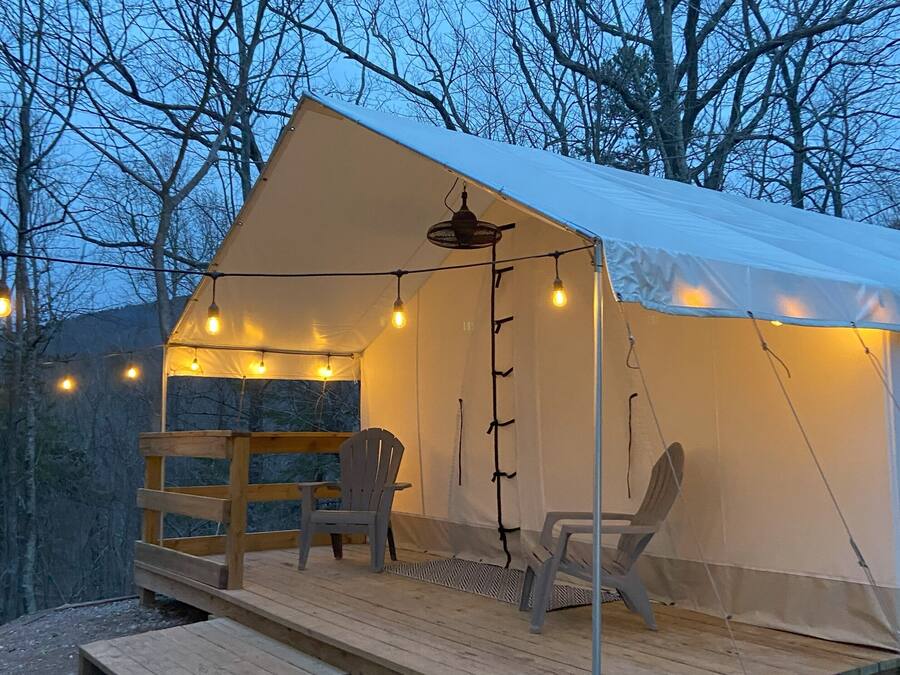 Una carpa con una terraza de madera, dos sillas y luces colgantes.
