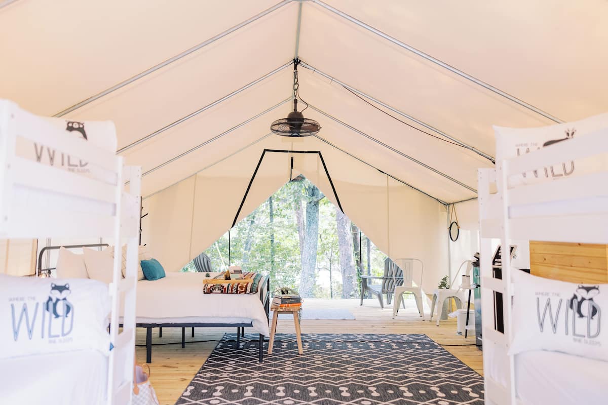 A tented accommodation with a bed, a small table, and a chair.
