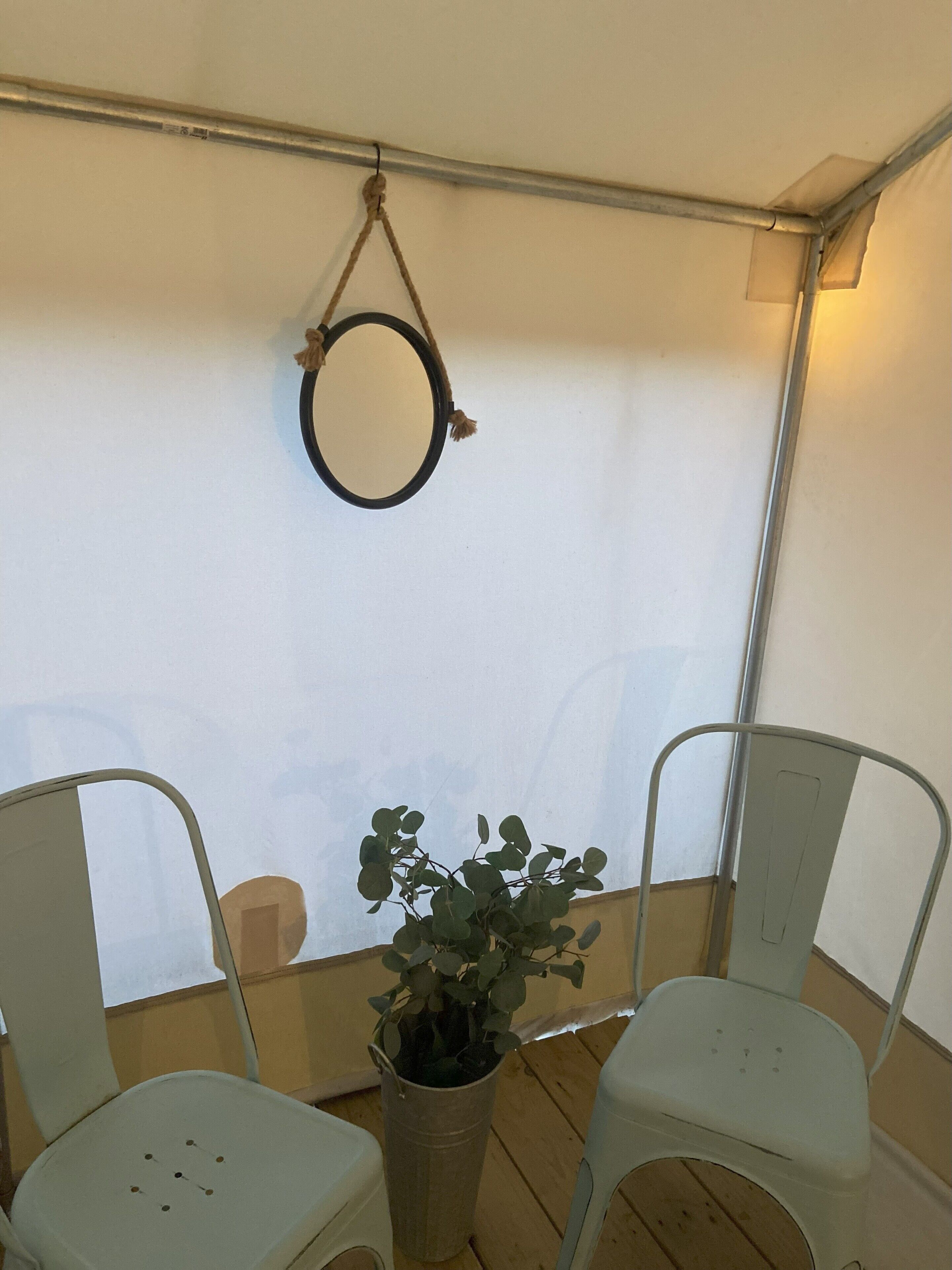 A small, enclosed outdoor seating area with two white chairs and a potted plant.