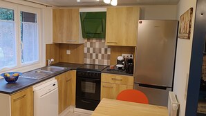 A compact kitchen with wooden cabinets, a dishwasher, a stove, and a refrigerator. - Studio à Louer (Clohars-Carnoët)