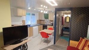 A compact living space with a kitchenette, dining area, and a TV on a wooden stand. - Studio à Louer (Clohars-Carnoët)