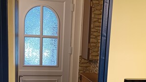 A room with a wooden floor, a white door with a frosted glass window, a stone wall, and a small table with a chair. - Studio à Louer (Clohars-Carnoët)