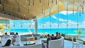 Ein moderner Lounge-Bereich mit einer geschwungenen Sitzgruppe, großen Fenstern mit Meerblick und einer hohen Decke mit hängenden Lampen.