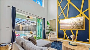 A modern living room with a grey sofa, a blue rug, a wooden coffee table, and a yellow geometric wall design. - 9 Miles to Disney: Themed Rooms, Pool & Theater (Kissimmee)