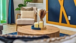 A round wooden coffee table with candles and a decorative vase, a beige armchair with patterned cushions, and a large wall decoration. - 9 Miles to Disney: Themed Rooms, Pool & Theater (Kissimmee)