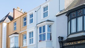 Uma fileira de edifícios de vários andares com estilos arquitetônicos distintos, incluindo um edifício com uma placa que diz 'CYCLES, MOTORS'.