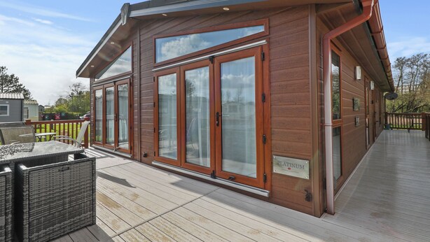 A wooden building with large glass doors and windows, a deck, and a sign that reads "PLATINUM." - Cormorant - Luxury Lodge, Close to the Beach (Tenby)