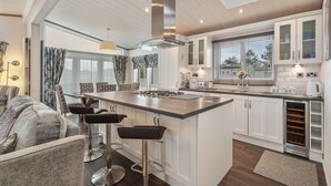 A modern kitchen with a central island, bar stools, white cabinetry, and a skylight. - Cormorant - Luxury Lodge, Close to the Beach (Tenby)