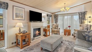 A cozy living room with a fireplace, comfortable seating, and a television. - Cormorant - Luxury Lodge, Close to the Beach (Tenby)