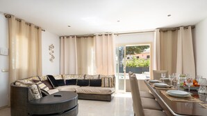 A modern living room with a sectional sofa, a round coffee table, and a dining area with a table set for four. - Villa Hilary with private pool near Playa de Muro (Muro)