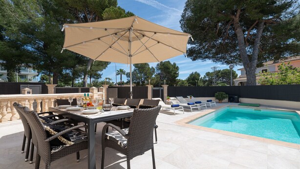 Un espace extérieur aménagé pour les repas, avec une piscine, des chaises en osier et une table dressée.