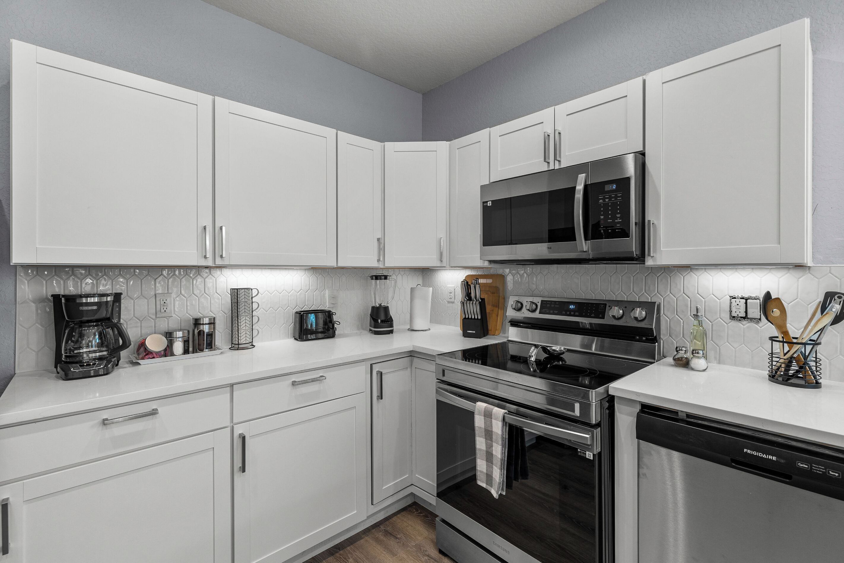 Una cocina moderna con gabinetes blancos, electrodomésticos de acero inoxidable y salpicadero de azulejos.