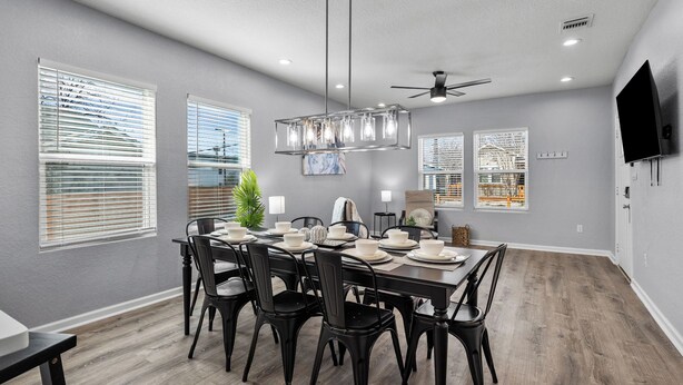 Un espace repas avec une table rectangulaire dressée pour quatre personnes, entourée de chaises noires, sous un luminaire suspendu au design moderne.