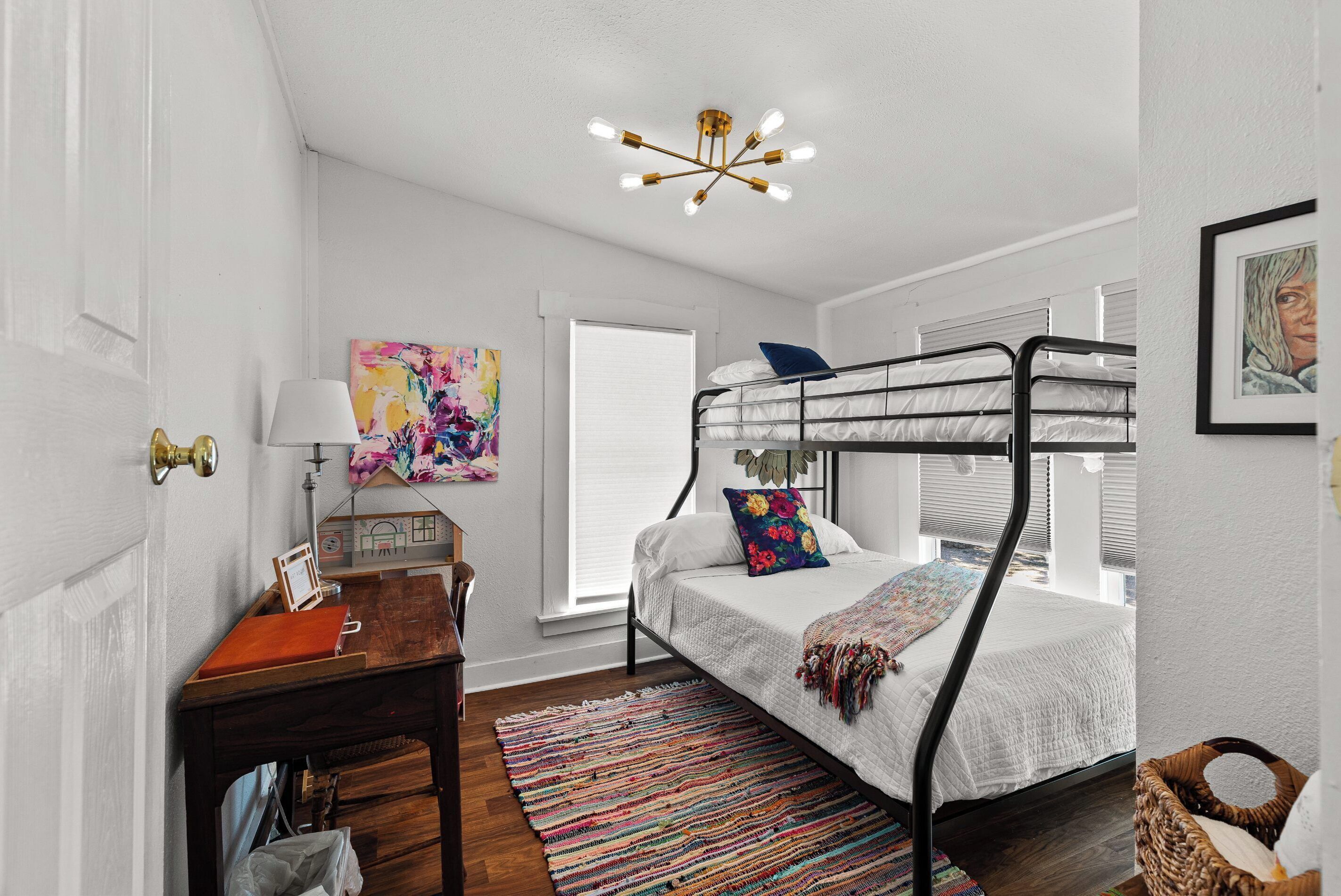 Une chambre avec un lit superposé, un bureau en bois, un tapis coloré et un luminaire au plafond.