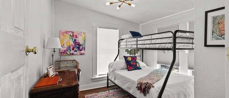 Une chambre avec un lit superposé, un bureau en bois, un tapis coloré et un luminaire au plafond.