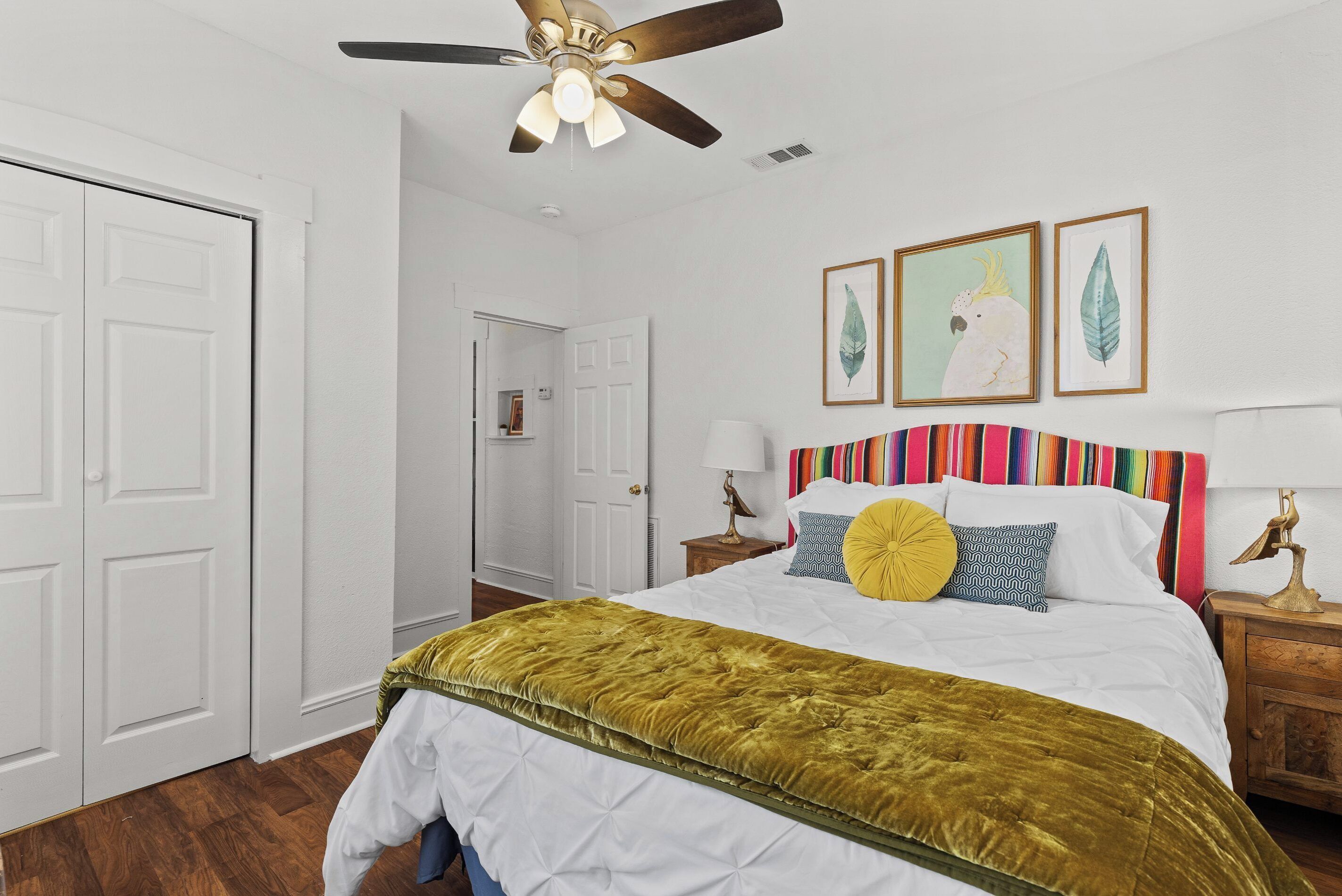 A bedroom with a bed, a ceiling fan, a nightstand, and a door.