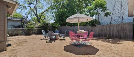 A backyard with a patio area featuring a table and chairs, an umbrella, and a wooden fence.