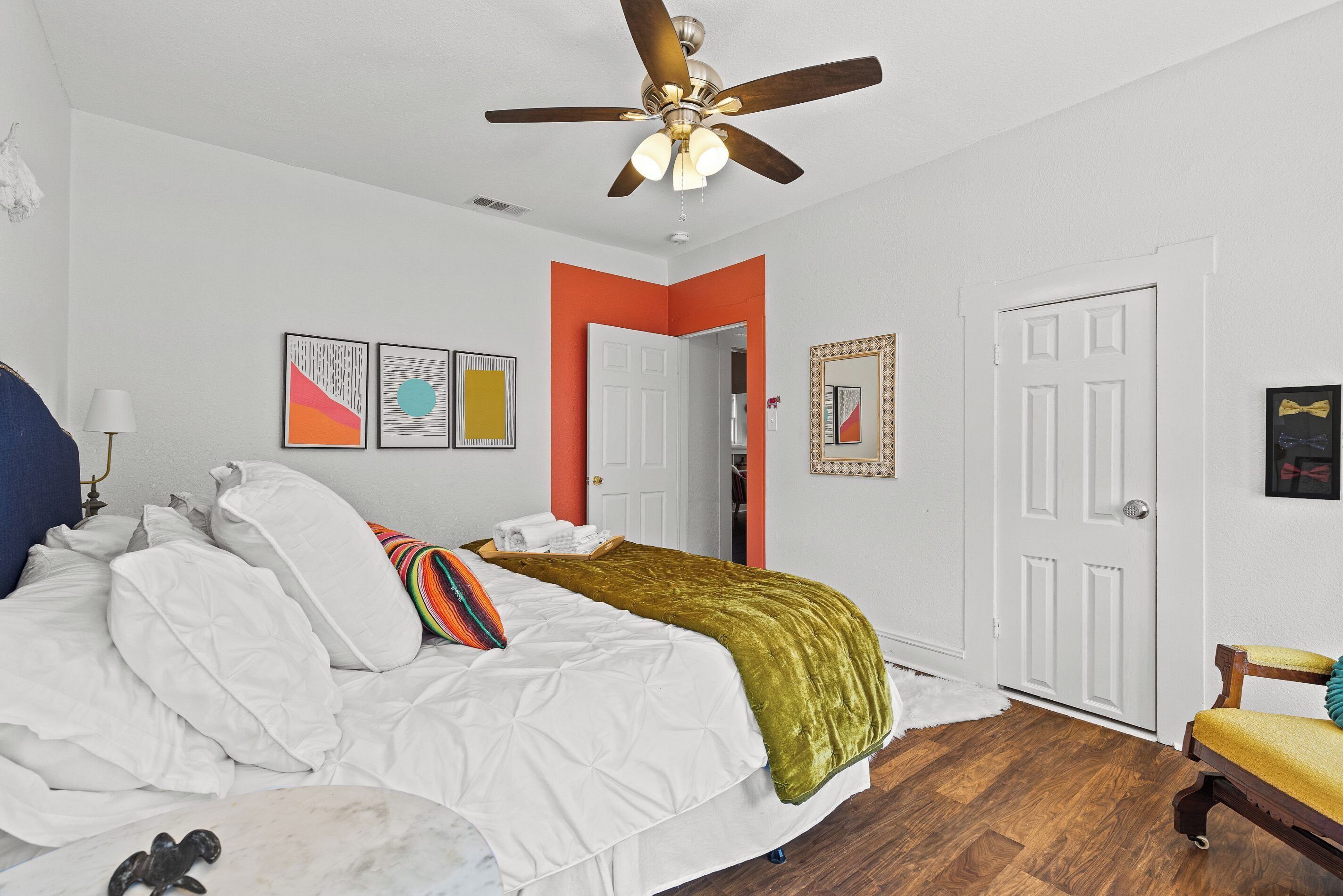 A bedroom with a bed, white walls, a ceiling fan, and a wooden floor.