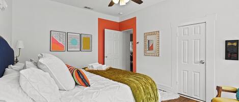 A bedroom with a bed, white walls, a ceiling fan, and a wooden floor.
